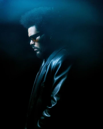 Profile portrait of The Weeknd wearing sunglasses and a black leather jacket against a moody blue background by Brian Ziff
