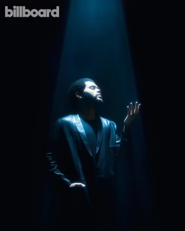 The Weeknd standing under a theatrical spotlight wearing a black leather jacket against a dark background