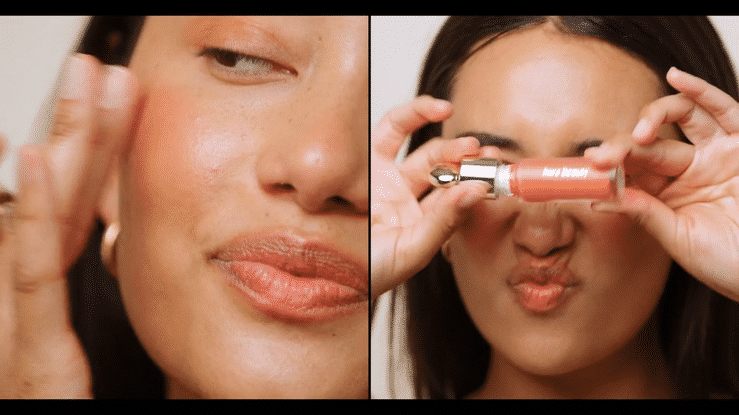 Woman applies blush in a beauty product demonstration with bright, even lighting and a soft focus in a close-up studio shot.