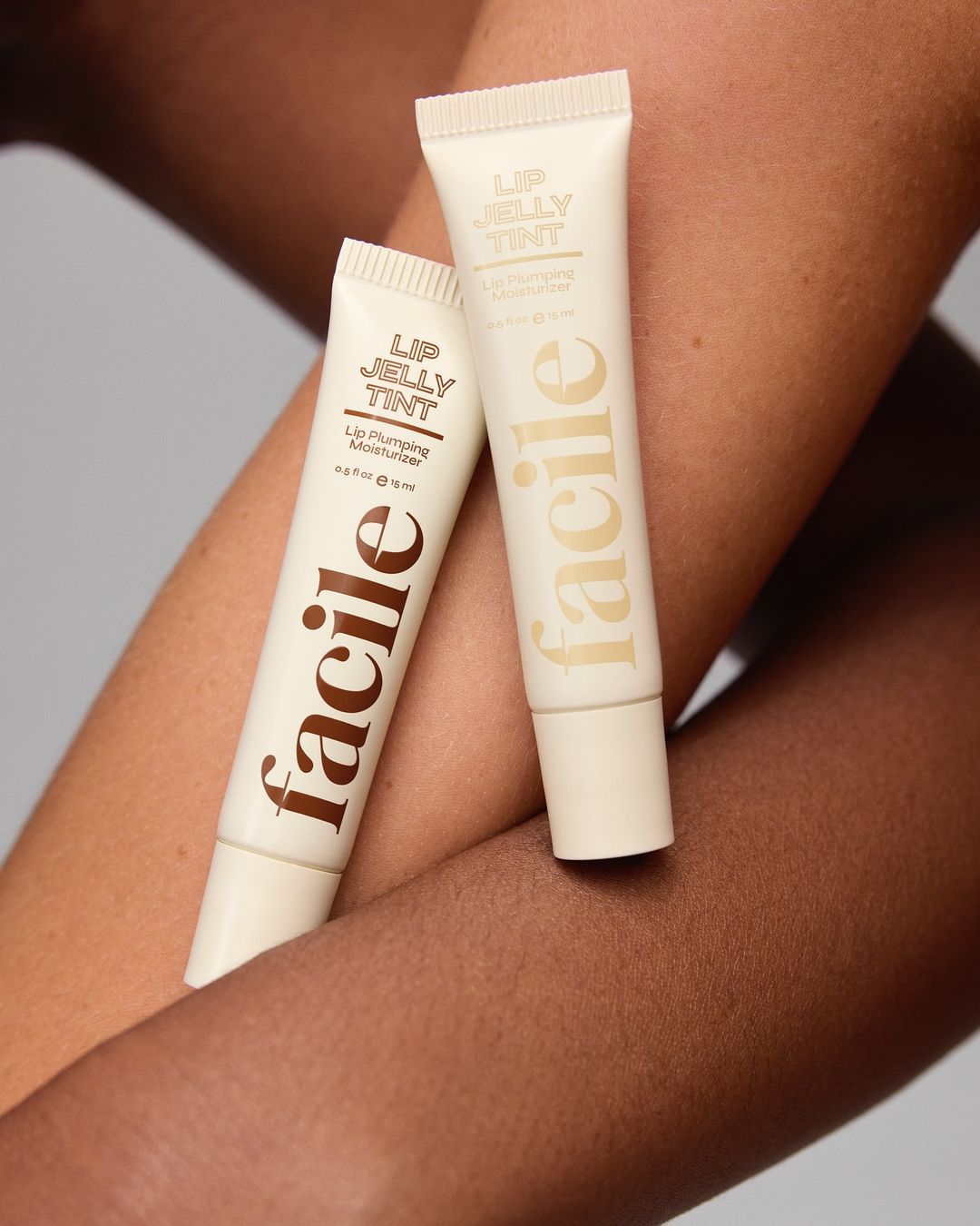 Two tubes of Facile Lip Jelly Tint moisturizer product resting on a lightly tanned arm in a beauty and skincare product shot.
