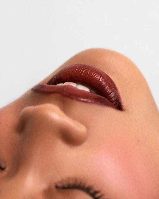 Close-up of a woman's face with her eyes closed and burgundy lipstick, emphasizing beauty and skincare in a minimalist, light-toned setting.