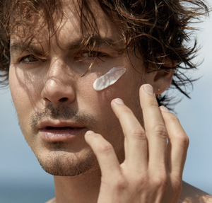 Close-up of a man applying sunscreen to his face near the ocean. Cosmetic product application with hand.