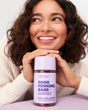 A smiling woman poses indoors with Bare Self Good Morning Babe Gummies, set against a pale lavender background.