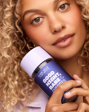 Close-up of a fair-skinned woman holding a bottle of Babe Self Good Night, Babe gummies, with a light purple background and soft lighting.