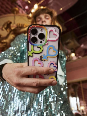 Close-up of a person holding a smartphone with a heart pattern case, wearing a sparkling sequin top.