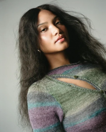 Portrait of a woman with long dark wavy hair wearing a striped knit top against a plain light background.
