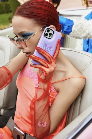 Woman with red hair poses in a car, holding up a purple cell phone with butterfly graphic. She wears sheer red gloves.