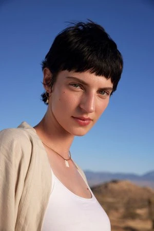 Portrait of a woman with dark short hair and a white top outdoors against a clear blue sky by Claire Leahy