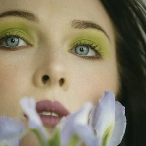 Close-up portrait of a woman with vibrant yellow eyeshadow and blue eyes holding pale blue flowers in Los Angeles by Claire Leahy.
