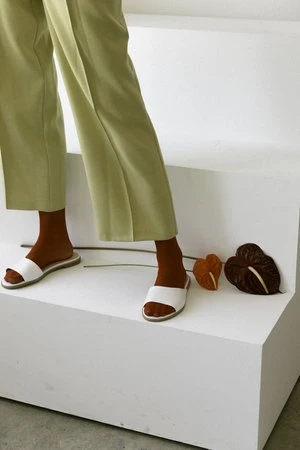 Woman wearing red socks and white slide sandals, standing on a white platform next to two Anthurium flowers.