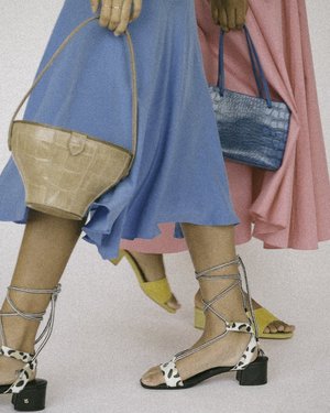 Close-up of two women in blue and pink dresses, carrying handbags, with eye-catching sandals, showcasing a blend of fashion and style.