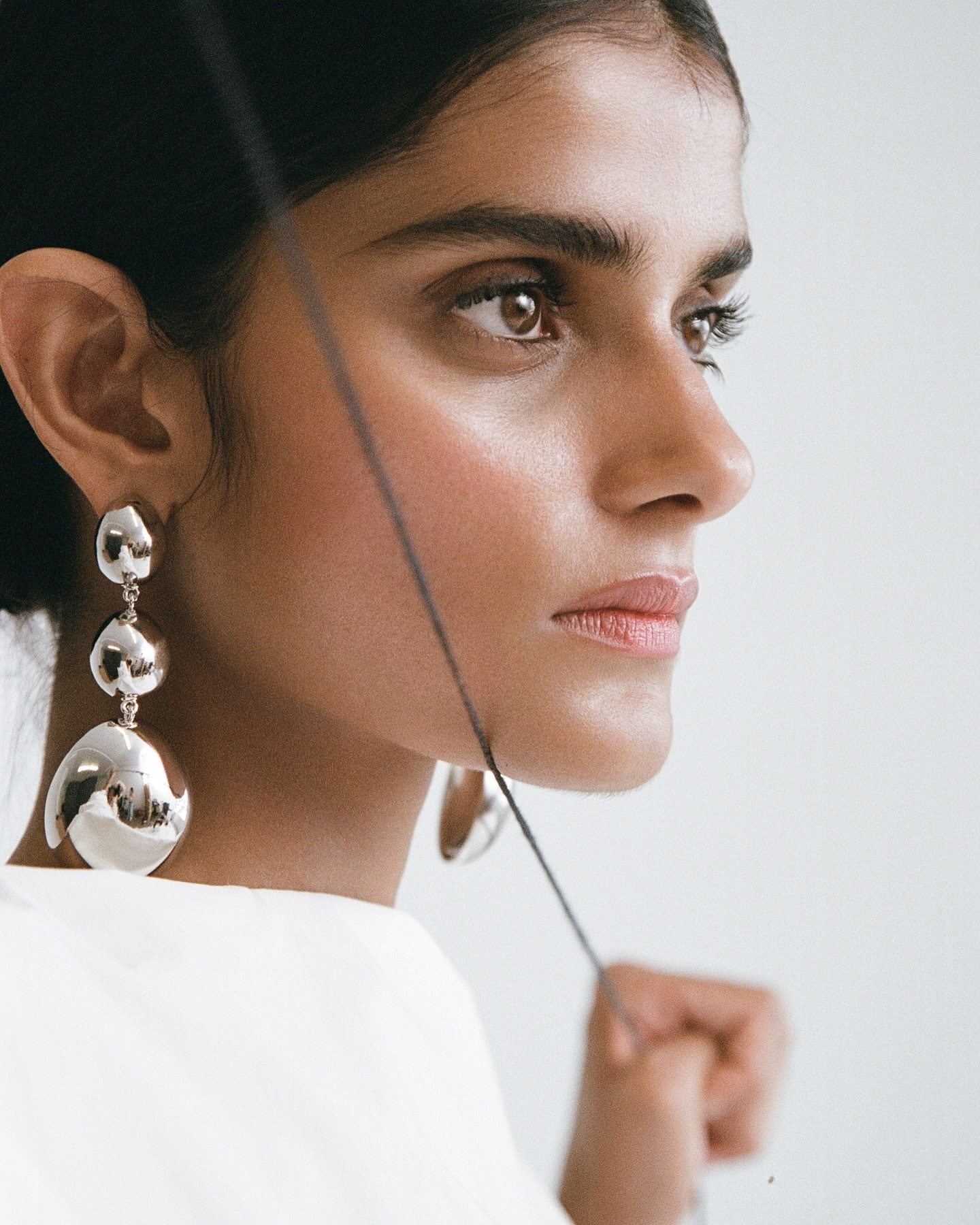 Close up profile portrait of a woman wearing large sculptural silver drop earrings and a white top by photographer Claire Leahy