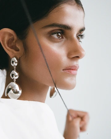 Close up profile portrait of a woman wearing large sculptural silver drop earrings and a white top by photographer Claire Leahy