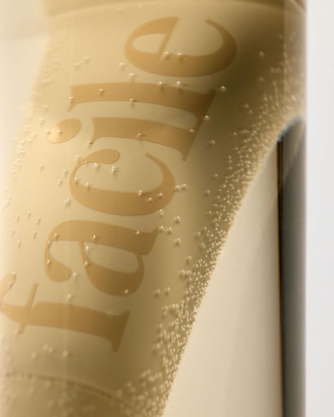 Close-up of a glass bottle with condensation and the word 'Facile' in a light tan color on the bottle against a white background.