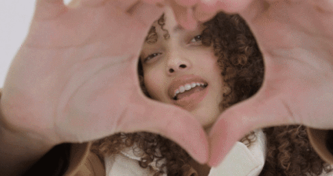 Young woman with curly hair looking through a heart shape formed by her hands in Los Angeles