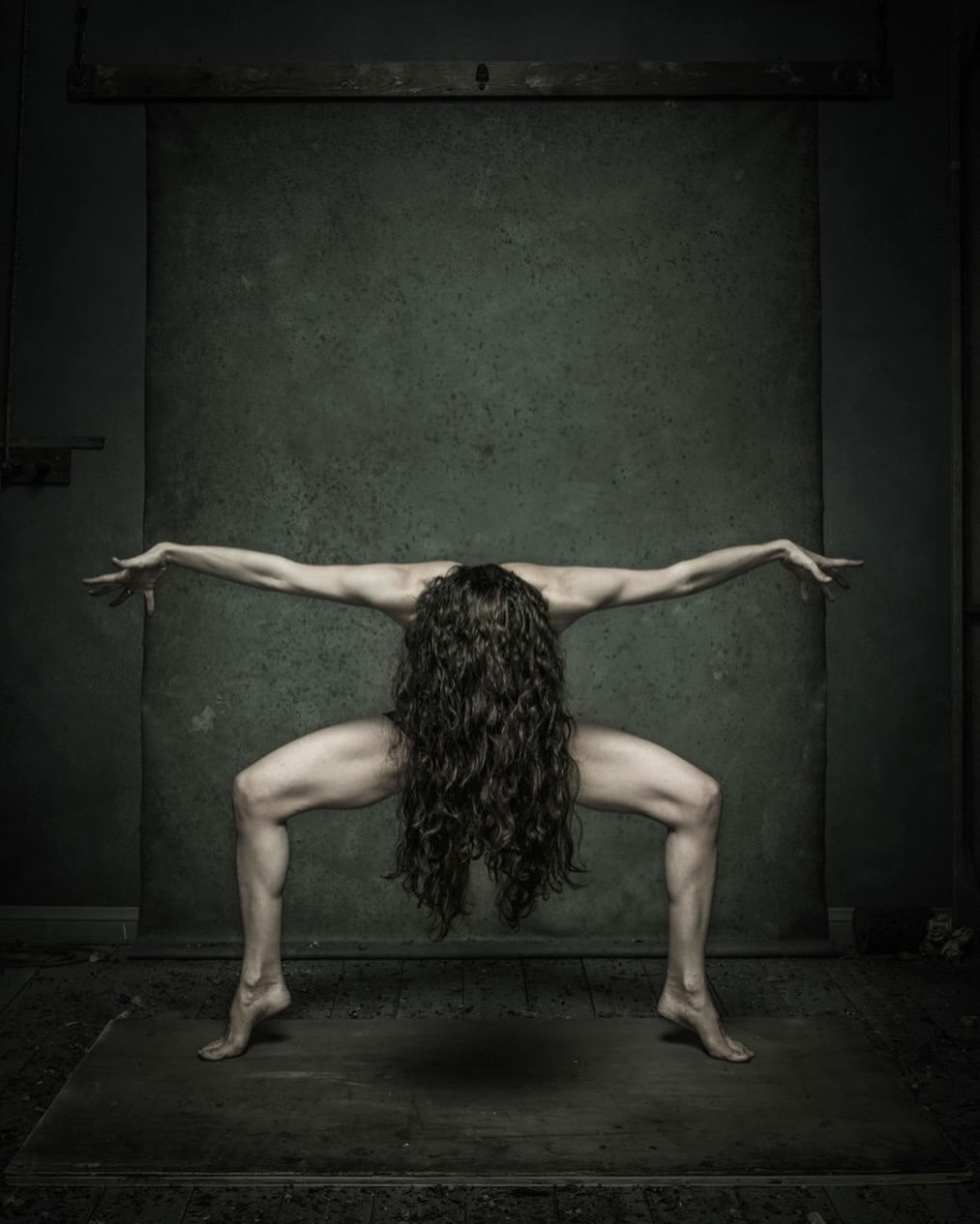 Abstract studio shot of a woman with long, dark hair, striking a pose in front of a muted green backdrop, with a dramatic, artistic flair.