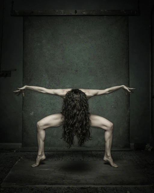Abstract studio shot of a woman with long, dark hair, striking a pose in front of a muted green backdrop, with a dramatic, artistic flair.