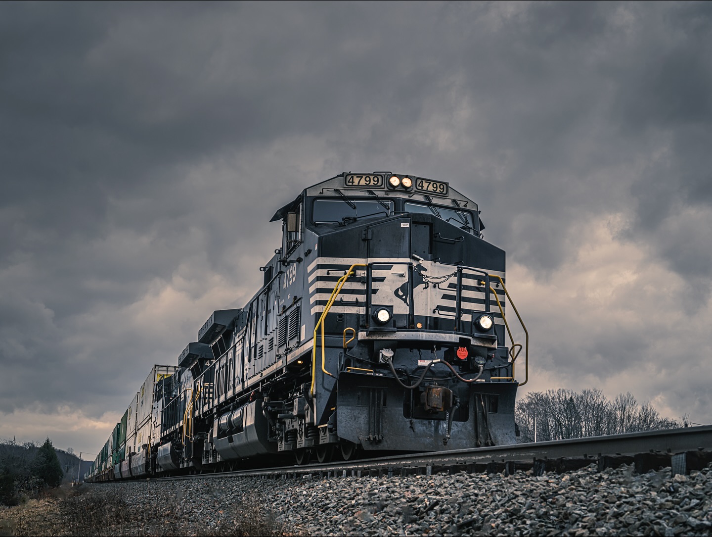 A black and silver locomotive train with the number 4799 travels on tracks under a cloudy sky, providing a powerful industrial image.