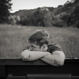 Monochrome portrait of a young man resting his crossed arms on a truck tailgate with a field and rolling hills in the background.