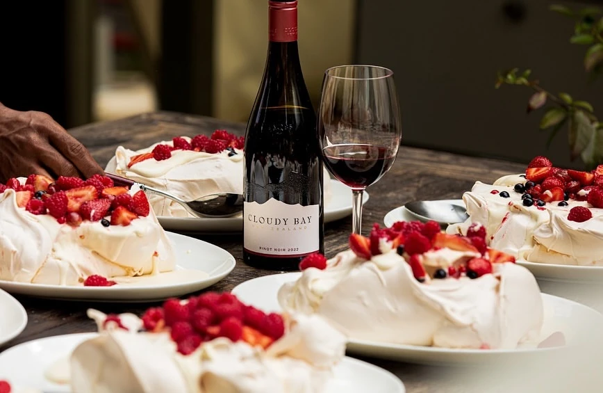 Wine and dessert still life: wine bottle and glass with pavlova cakes topped with fresh strawberries and raspberries on rustic wooden table.