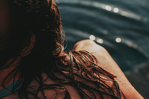Close-up shot of wet brown hair with dark blue water in the background with bokeh highlights.