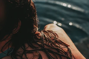 Close-up shot of wet brown hair with dark blue water in the background with bokeh highlights.