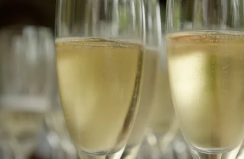 Close-up of champagne flutes filled with bubbly golden champagne, set against a blurred backdrop of more glasses.