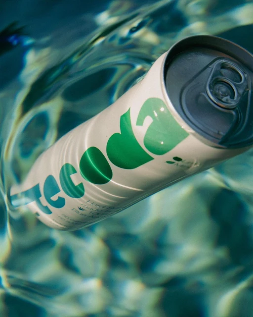 A white soda can with green lettering floating in rippled pool water. The brand name 'teecoda' is prominently displayed on the can.