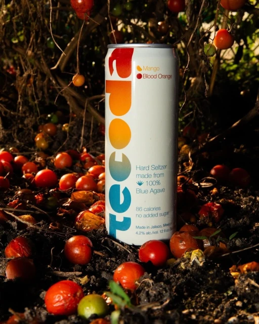A can of hard seltzer stands in the foreground, surrounded by red tomatoes and natural elements, with the brand name prominently displayed.