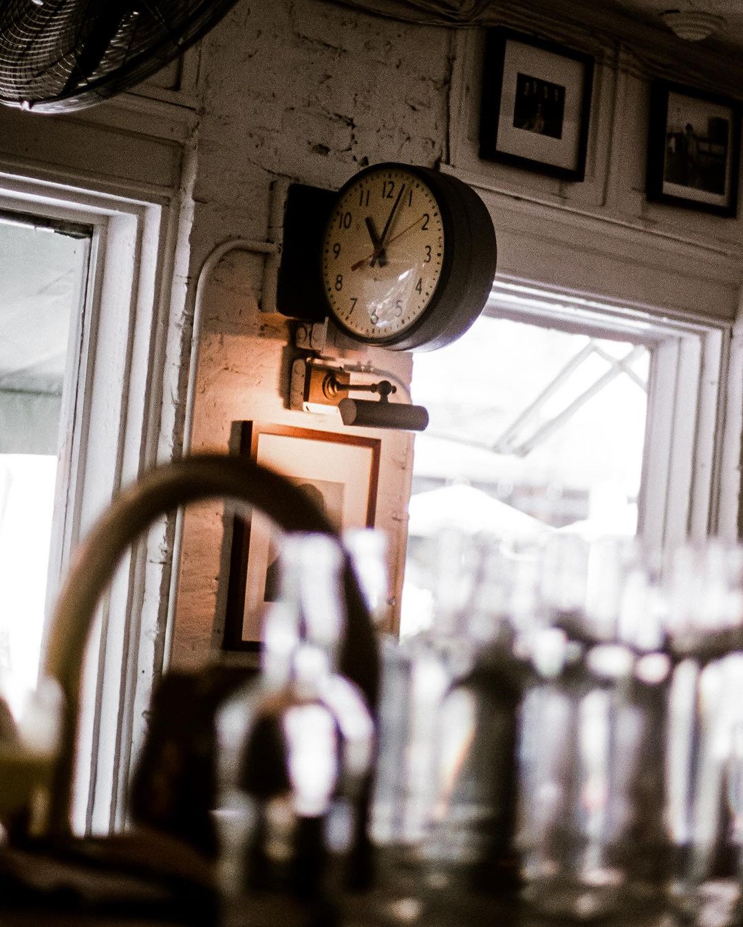 Indoor scene showcasing a vintage wall clock mounted on a white brick wall with a small lamp, accompanied by glassware.