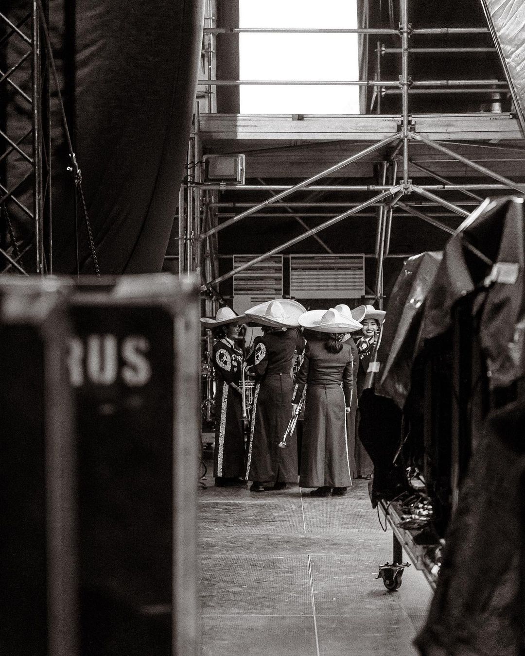 A black and white shot showcases a mariachi band in traditional charro attire standing on a stage, framed by scaffolding.