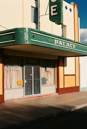 The Palace building exterior features a green awning, cream and tan tiled walls, and a vintage sign, under a partly cloudy sky.