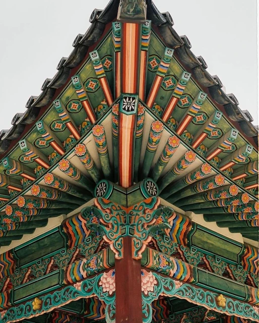 Close-up shot of the eaves and ornate paintings of a traditional Korean building featuring green, orange, and brown colors.