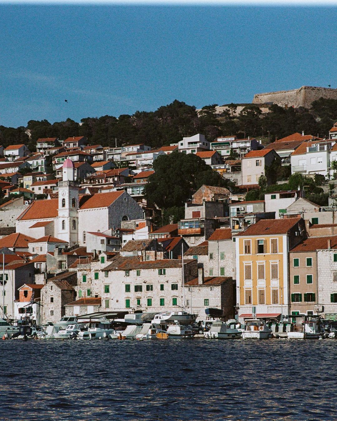 Coastal town with white buildings and red roofs, overlooking the blue ocean under a clear sky, showcasing European architecture.