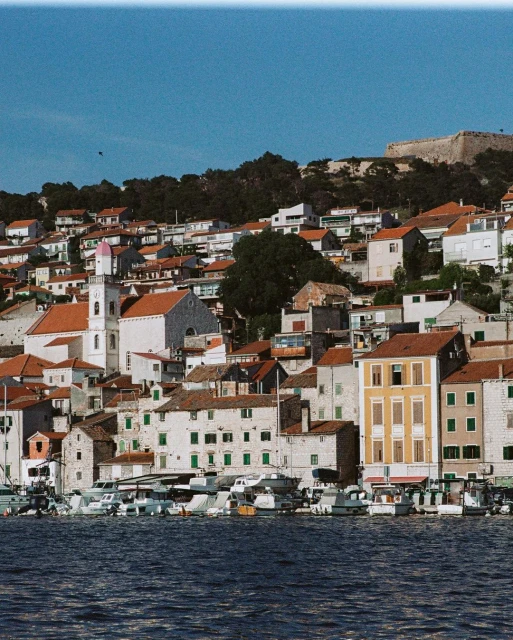 Coastal town with white buildings and red roofs, overlooking the blue ocean under a clear sky, showcasing European architecture.