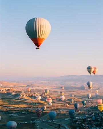 Hot air balloons float over a landscape at sunrise, creating a scenic view of Cappadocia, Turkey on a clear, sunny day.