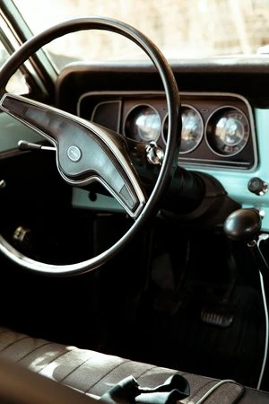Classic car interior view: steering wheel, dashboard gauges, and seat with seatbelt detail, capturing vintage automotive design.