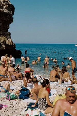 Candid shot of people relaxing and swimming on a rocky beach by the blue ocean by Lover Lover