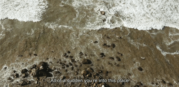 Aerial view of ocean waves washing onto a sandy beach with scattered rocks, offering a textured and natural coastal scene.