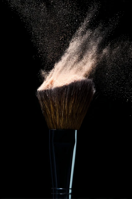 Close-up of a professional makeup brush loaded with loose powder against a stark black background, creating an impactful beauty image.
