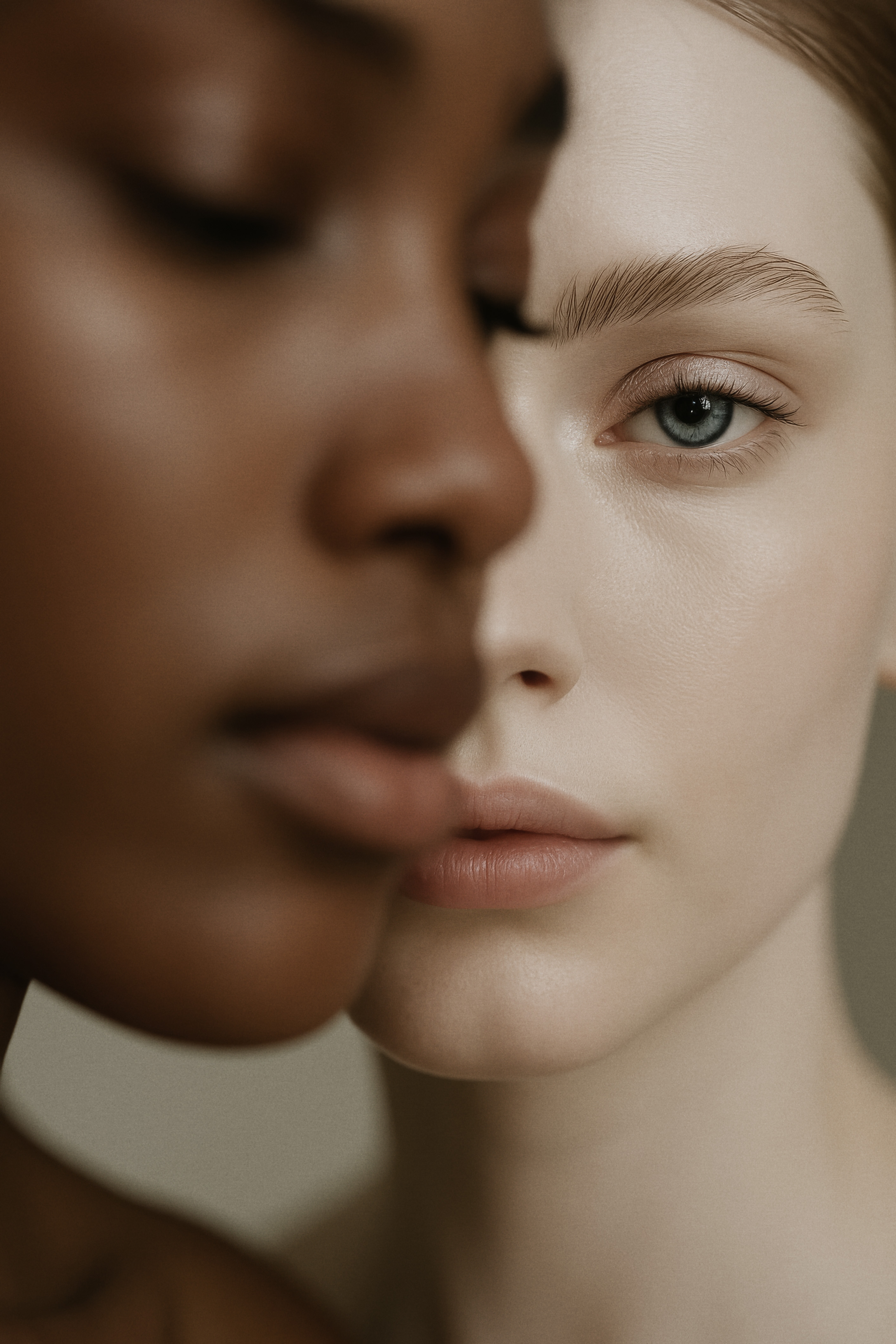 Close-up studio portrait of two diverse adult women with pale skin tones, focusing on their faces and contrasting complexions.