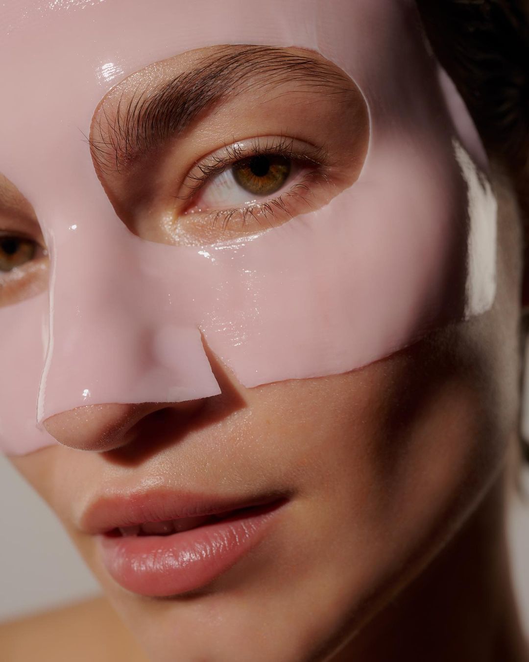 Close-up of a woman's face with a pink facial mask, highlighting skincare and beauty in a minimalist studio setting with soft lighting.