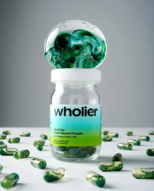 Close-up still life of a bottle of green-tinted multivitamin capsules, with loose capsules scattered around and a glass paperweight on top.