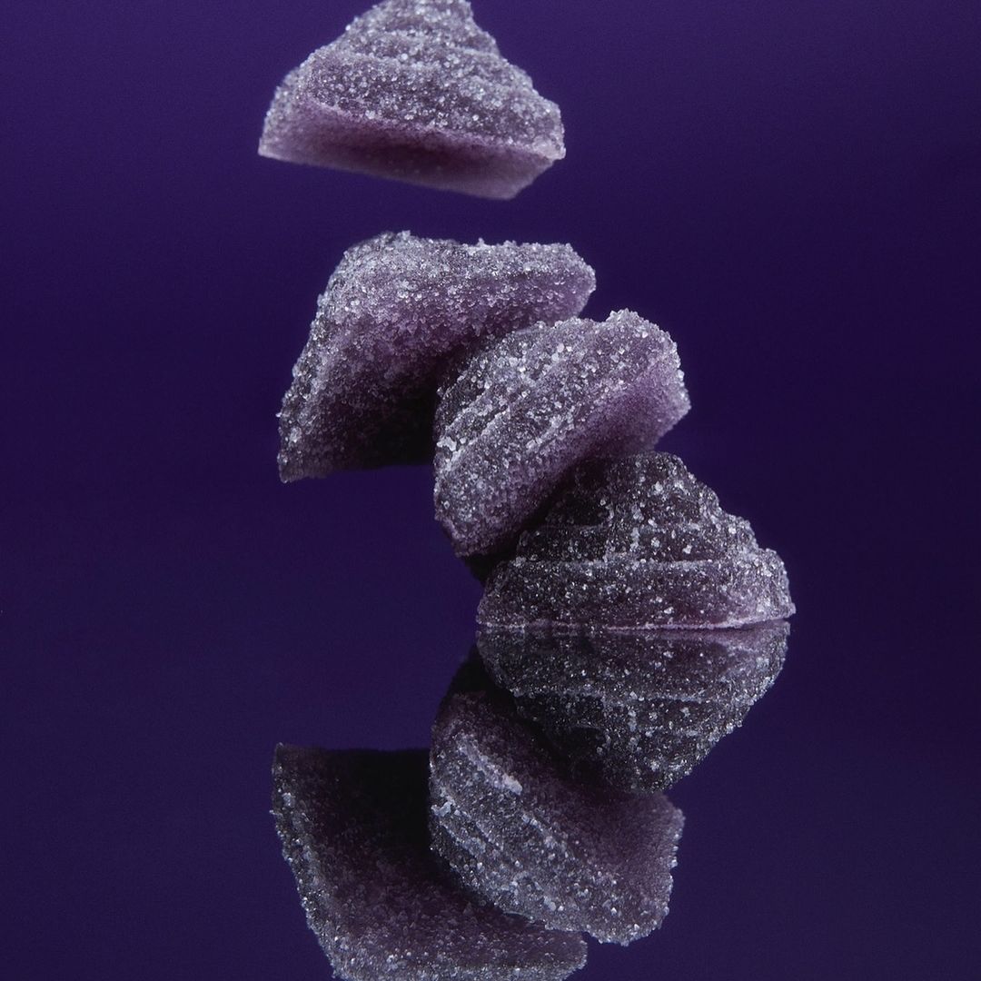 Stack of purple fruit jelly candies on a reflective surface against a purple background, showcasing the candy's texture and colour.