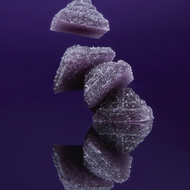 Stack of purple fruit jelly candies on a reflective surface against a purple background, showcasing the candy's texture and colour.