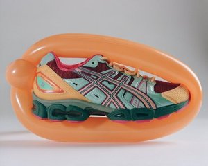 Close-up studio shot of a multicolored ASICS sneaker inside an inflated peach-colored balloon, set against a plain white background.