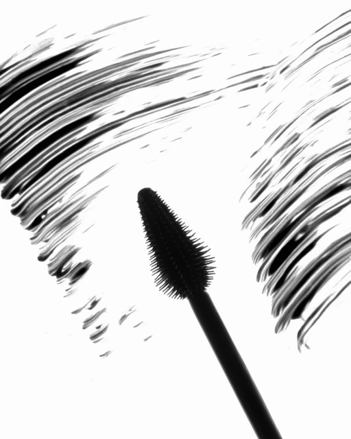 Macro shot of a black mascara brush and mascara smears on a white background, showcasing beauty and cosmetic application.
