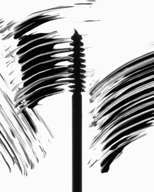 Close-up shot of a mascara brush with black mascara smeared around it, set against a bright white background, showcasing beauty product.