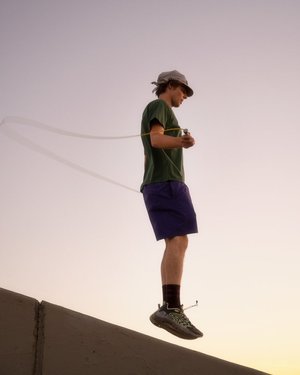 An athletic man in sportswear practices jump rope on a concrete ledge against a twilight sky, creating an image that highlights fitness.