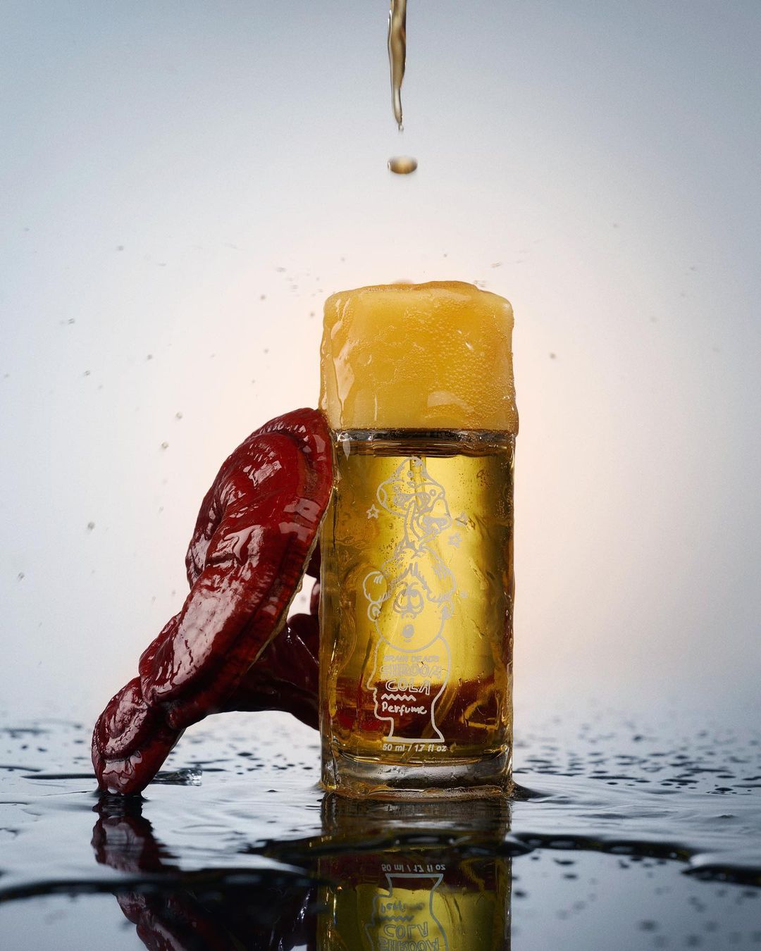 Perfume bottle with a red mushroom, golden liquid, and water droplets creating a refreshing and luxurious beauty or wellness visual.